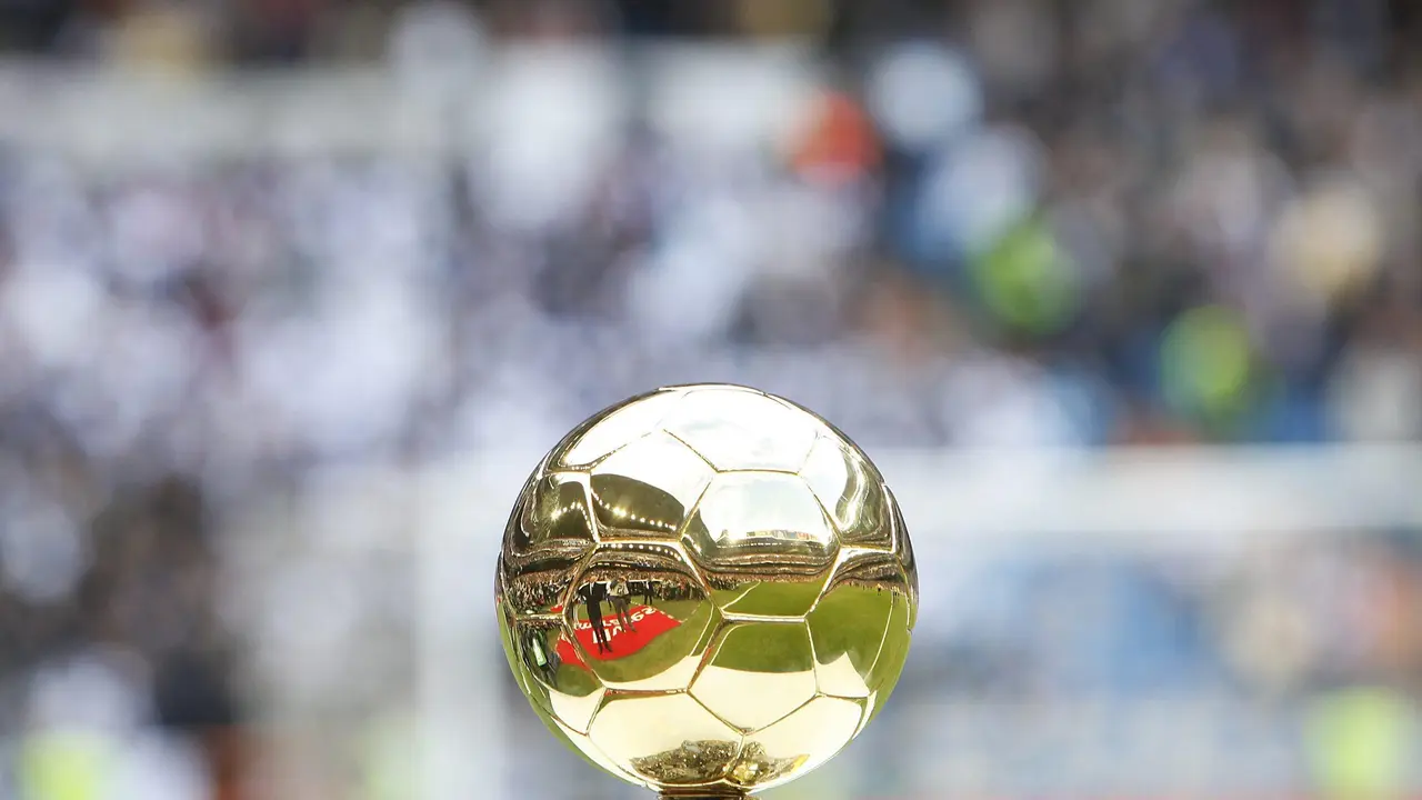 The golden Ballon d'Or trophy displayed against a blurred stadium background