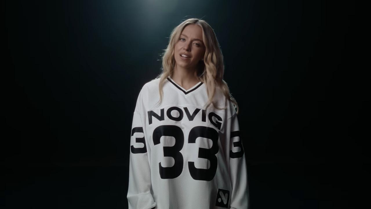 Sydney Sweeney in a Novig sports-advertisement still, wearing a white Novig jersey under studio lighting
