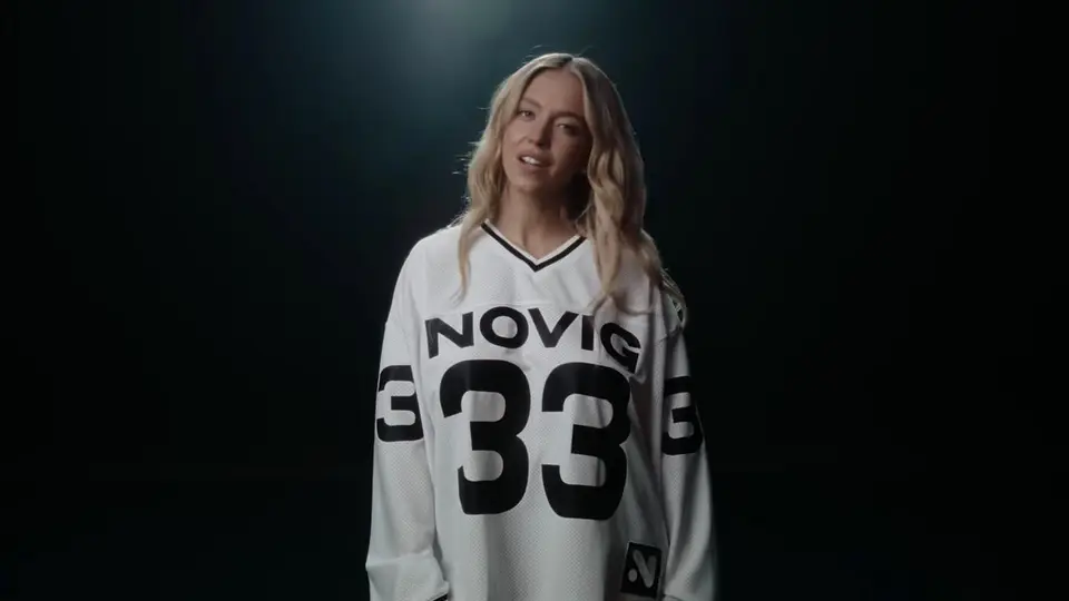 Sydney Sweeney in a Novig sports-advertisement still, wearing a white Novig jersey under studio lighting