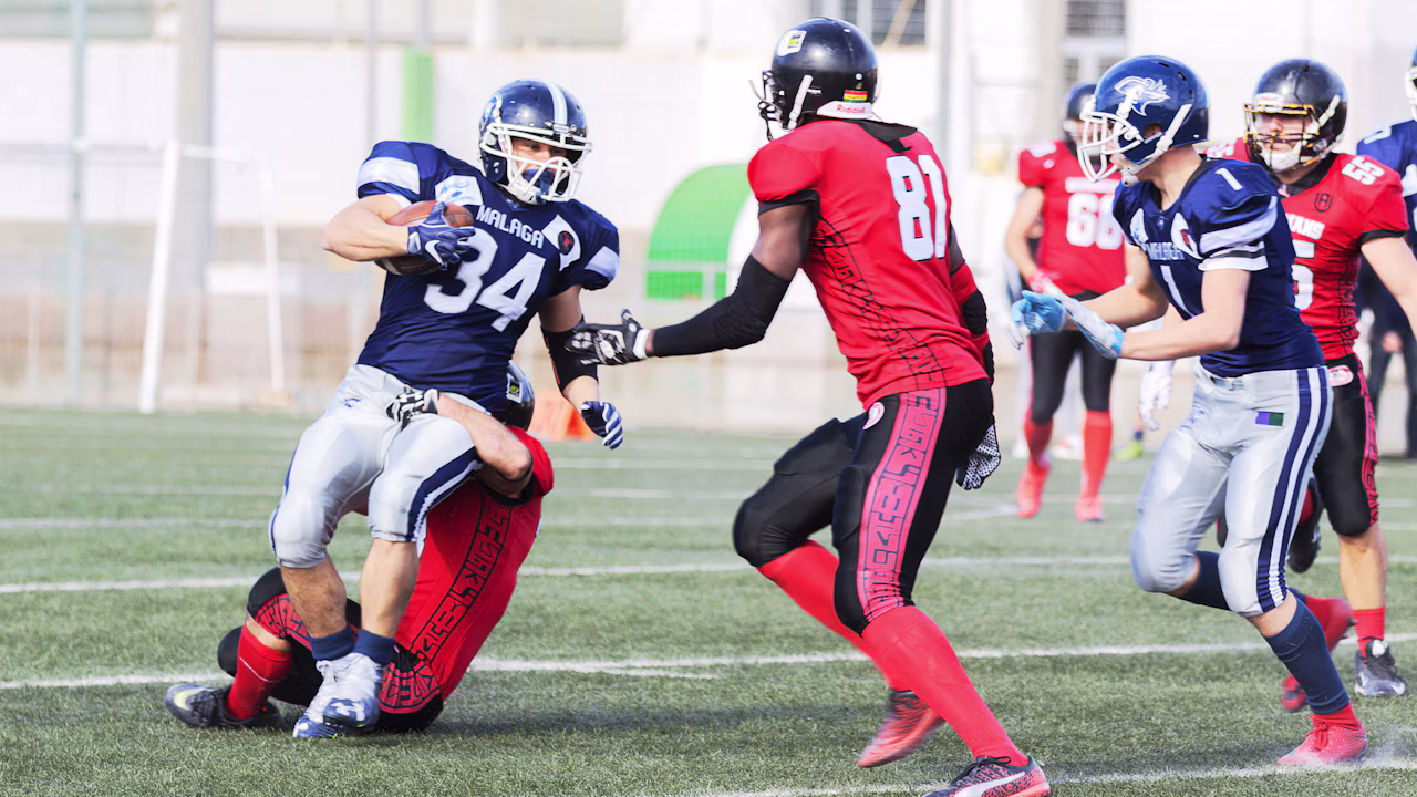 American football players clash on a grass field during a tackle
