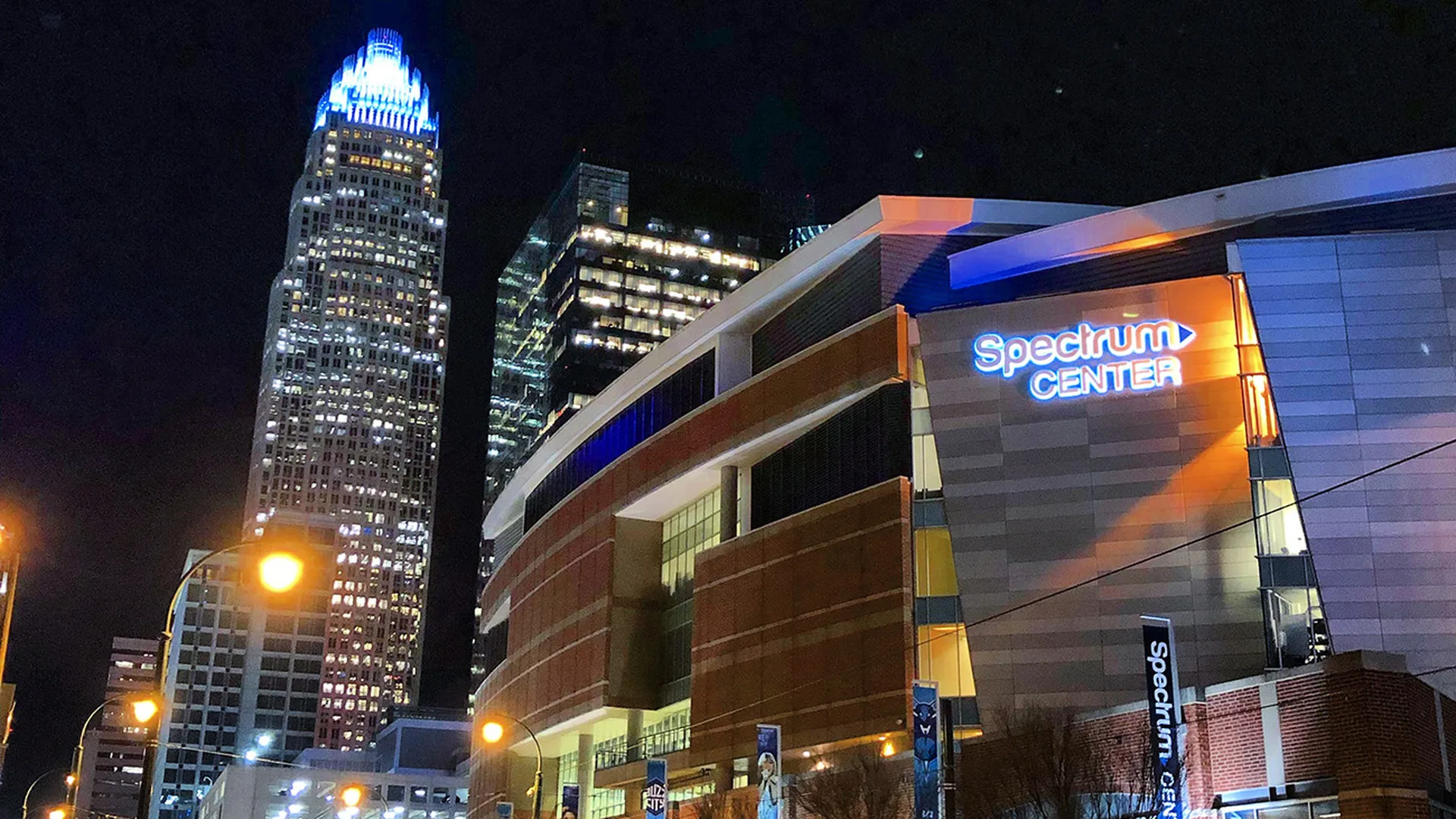 Spectrum Center, home of the Charlotte Hornets, illuminated against the Charlotte skyline at night
