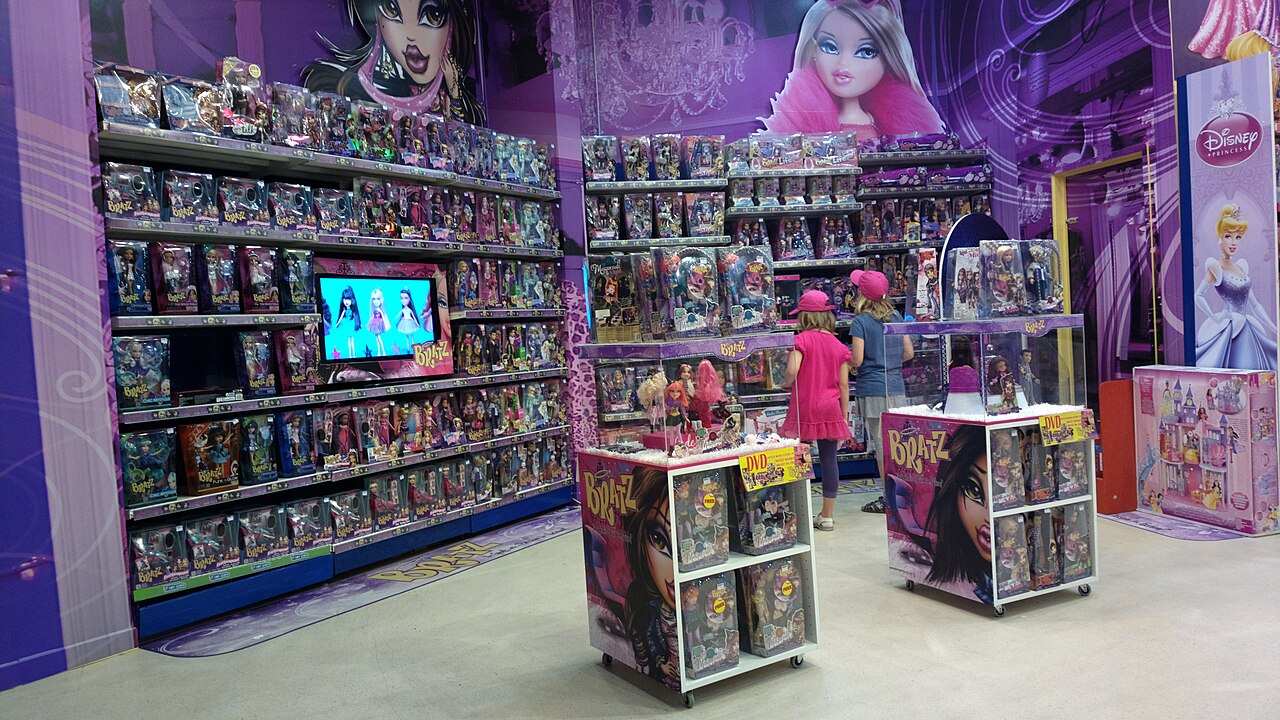 Shelves and display carts stocked with boxed Bratz dolls inside a purple-themed toy store section as two children browse