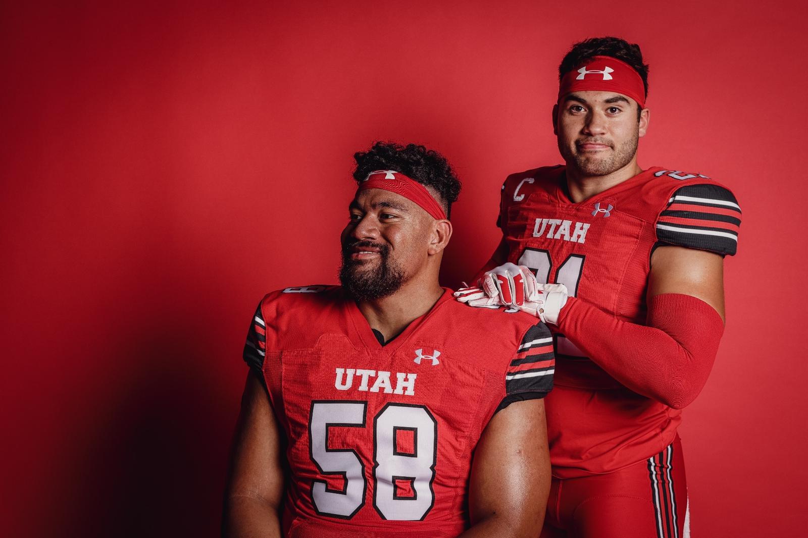 Two Utah football players in uniform pose in front of a red backdrop.