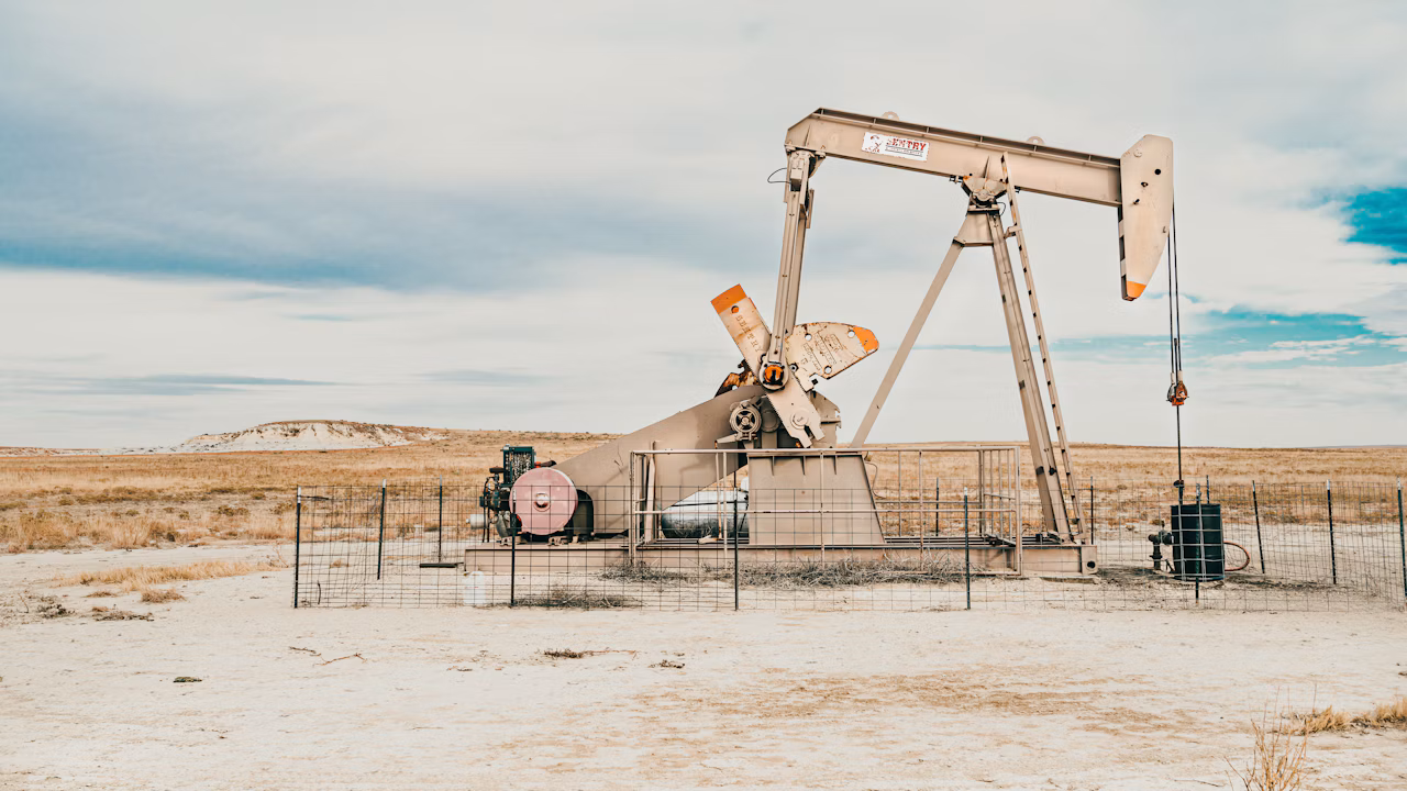 A pump jack stands on a sandy plain beneath an overcast sky.