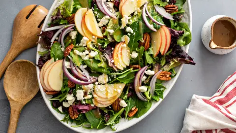 Mixed green salad topped with sliced apples, red onion, pecans and crumbled cheese