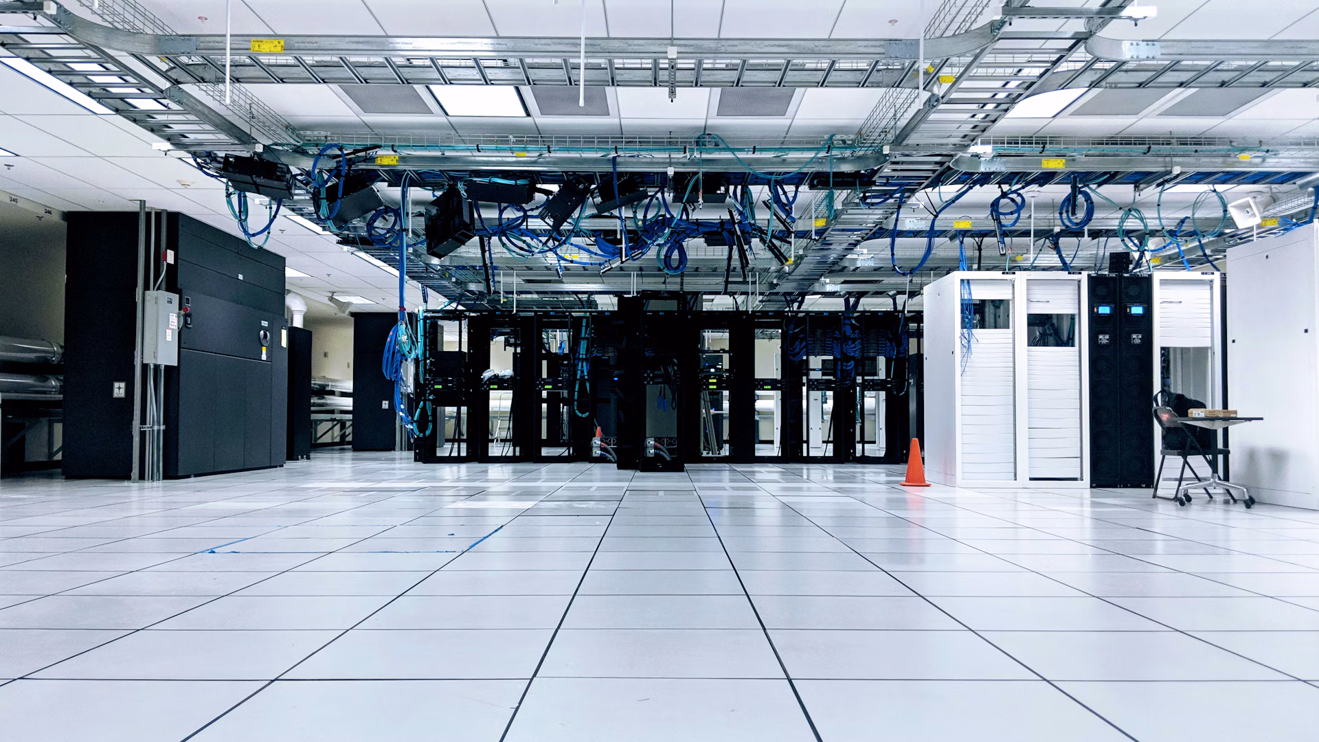 Server cabinets and overhead network cables in a data center; illustrative, not Anthropic’s facilities.