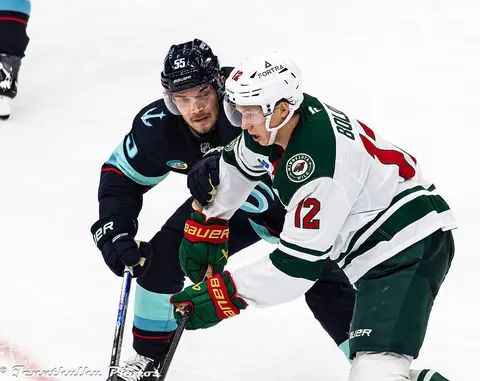 Minnesota Wild forward Matt Boldy, wearing number 12, skates with the puck while a Seattle Kraken defender in a dark jersey checks him, in a January 2026 game.