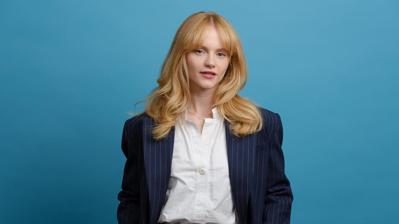 Actor Emma Laird poses in a navy pinstripe suit against a blue studio background