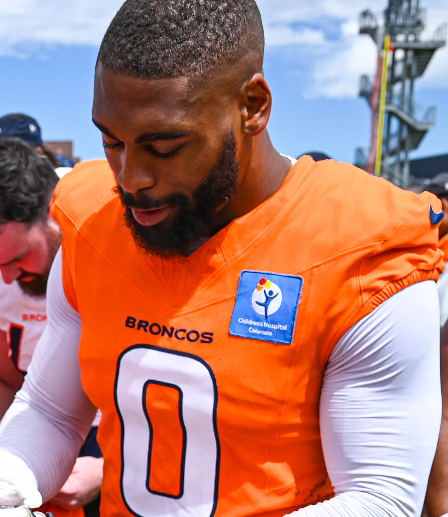 Jonathon Cooper in an orange Denver Broncos No. 0 practice jersey signing autographs at the team's facility in Englewood, Colorado, in August 2024
