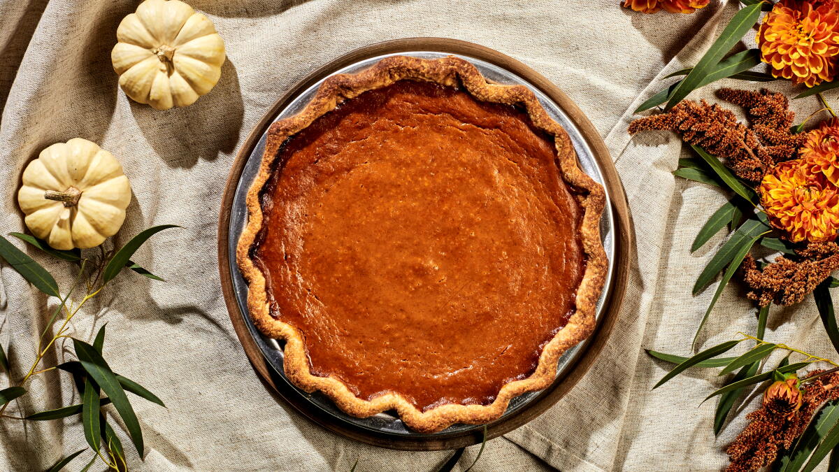 A golden pumpkin pie surrounded by small white pumpkins and autumn flowers on a Thanksgiving dessert table