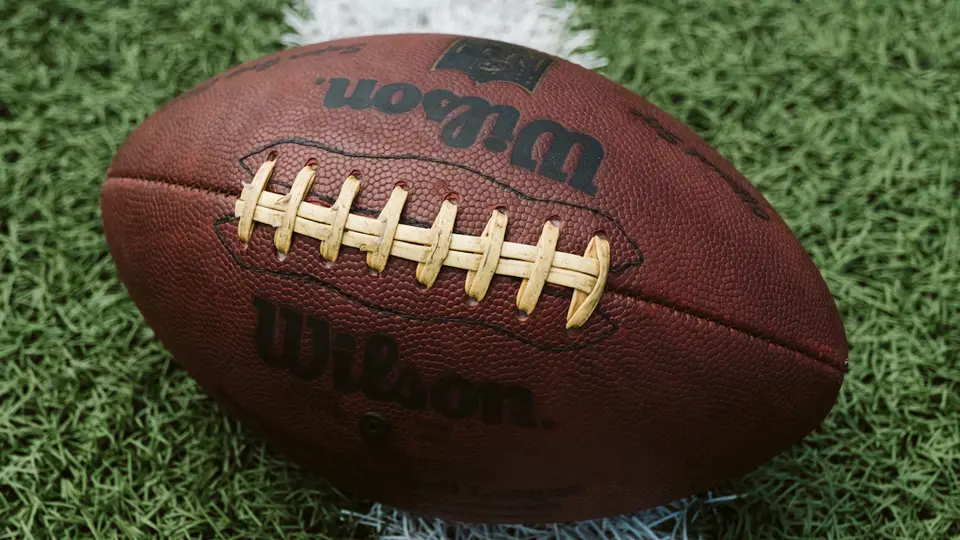 An American football rests on grass at a field
