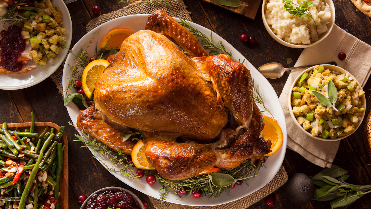 Roasted Thanksgiving turkey surrounded by stuffing, mashed potatoes, green beans and cranberry sauce