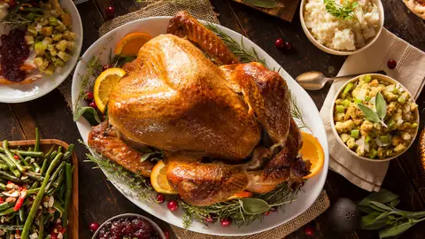Roasted Thanksgiving turkey surrounded by stuffing, mashed potatoes, green beans and cranberry sauce