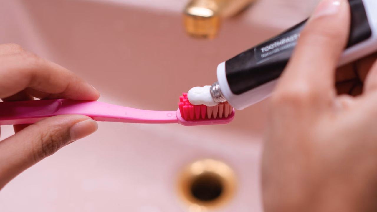 A person putting toothpaste on a toothbrush in a bathroom