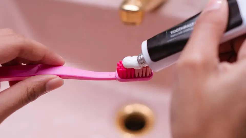 A person putting toothpaste on a toothbrush in a bathroom