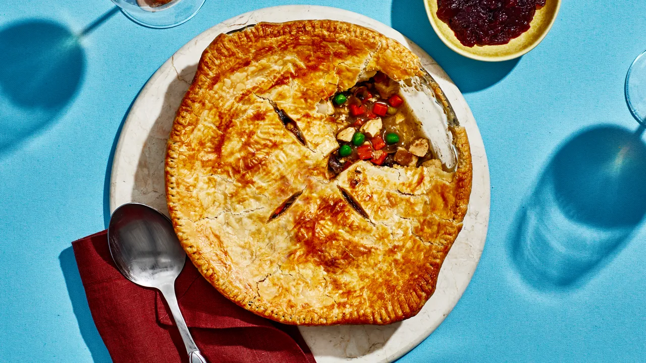 A golden turkey pot pie filled with turkey and vegetables beside cranberry sauce