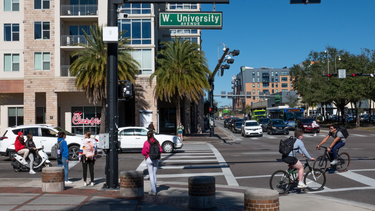 Pedestrians and cyclists cross West University Avenue at West 13th Street in Gainesville, Florida.