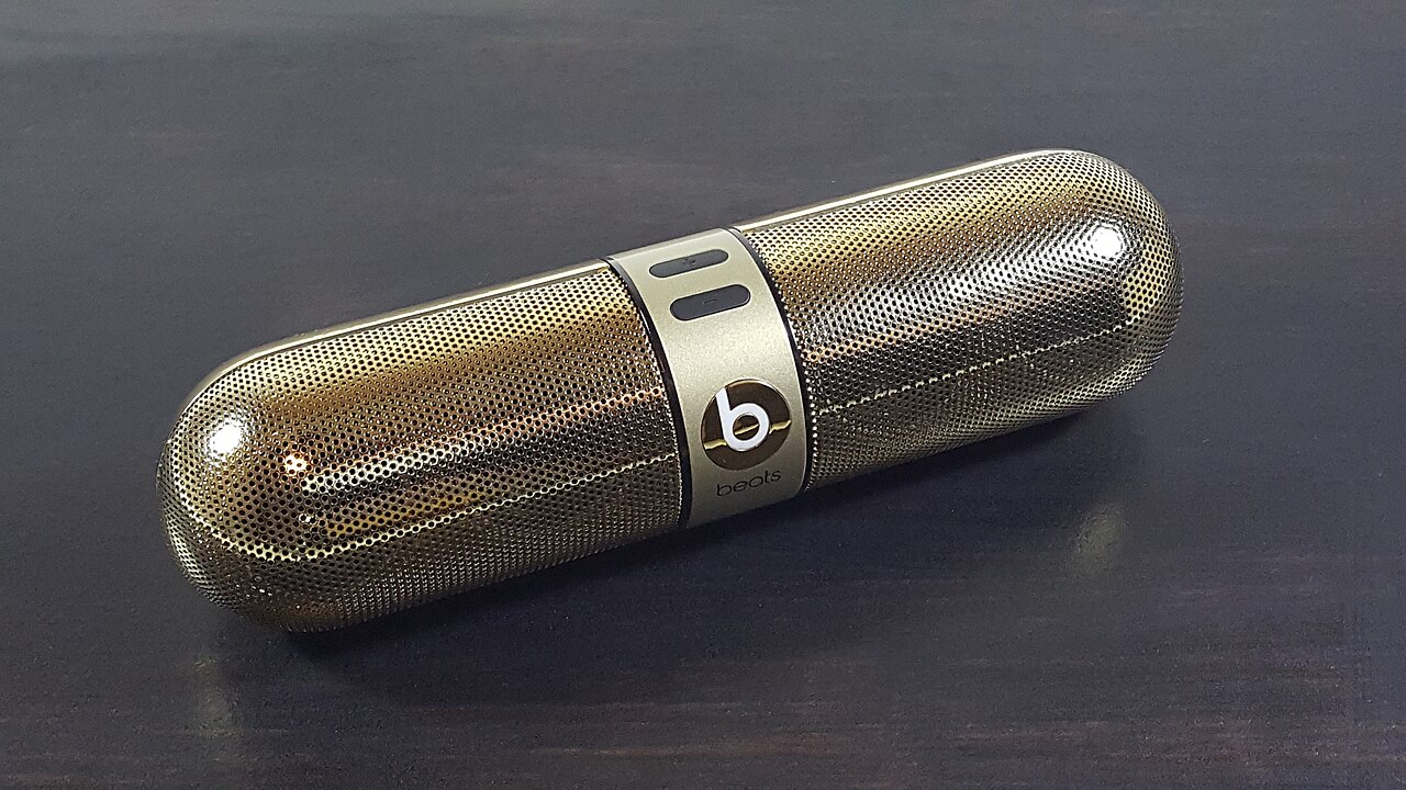 An earlier-generation Beats Pill portable Bluetooth speaker in a gold finish resting on a dark wooden table